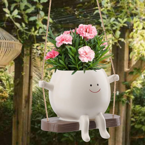 White planter with pink flowers on a swing in a garden setting